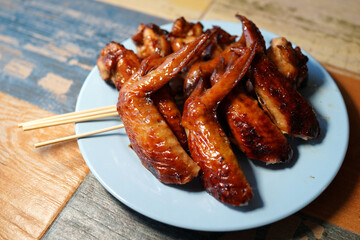 Grilled chicken wings in plate on wooden table. Soft focus image.