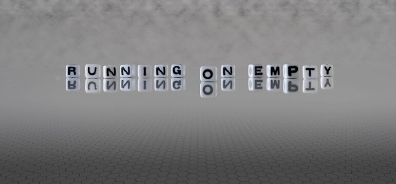 running on empty word or concept represented by black and white letter cubes on a grey horizon background stretching to infinity