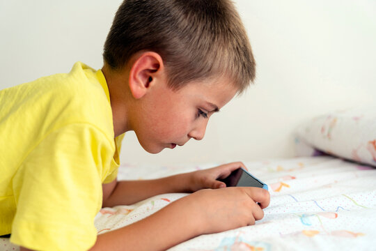 Kid lying on bed and playing videogame on smartphone