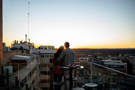 Anonymous couple standing on rooftop at sunset