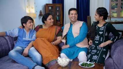 A happy Indian couple with their two kids chatting together in the living room - a small nuclear family  family bonding. A cheerful Bengali family in traditional clothes posing together for the cam...