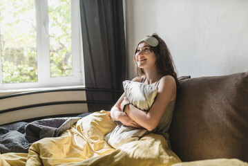 Portrait of young woman in sleeping mask holding pillow and lying in bed. Awakening in the morning. Happy good morning