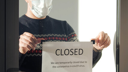 Owner of the institution hangs a closed sign on the window. Impact of the coronavirus in a business.