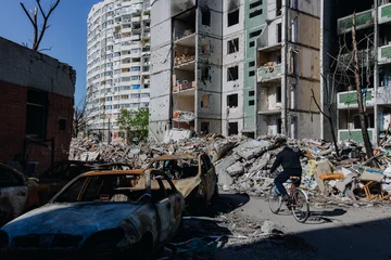 Gordijnen Chernihiv Ukraine 2022: A man rides a bicycle near a destroyed building and cars after an air strike. Ruins during Russia's war against Ukraine. © Maksym
