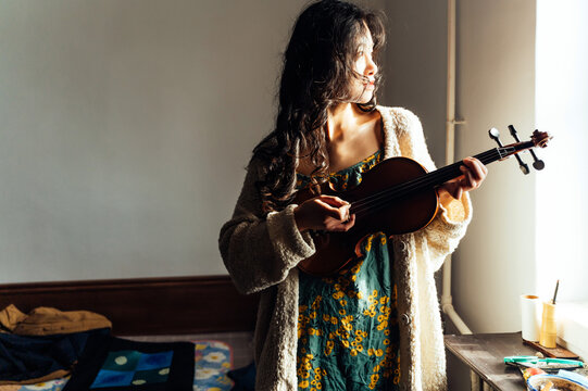 An asian young woman playing violin at home