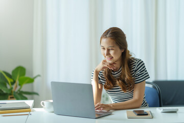 Portrait of young Asian business woman using laptop computer at home office.