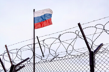 View of russian flag behind barbed wire against cloudy sky. Concept anti-Russian sanctions. border post on the border of Russia. cancel culture Russia in the world