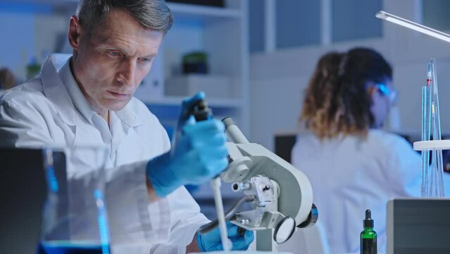 Chemist examining chemical substance sample under microscope, lab experiment