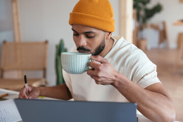 Black freelancer drinking hot beverage during work