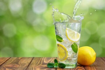 lemonade pouring in glass on wooden table with green blurred background