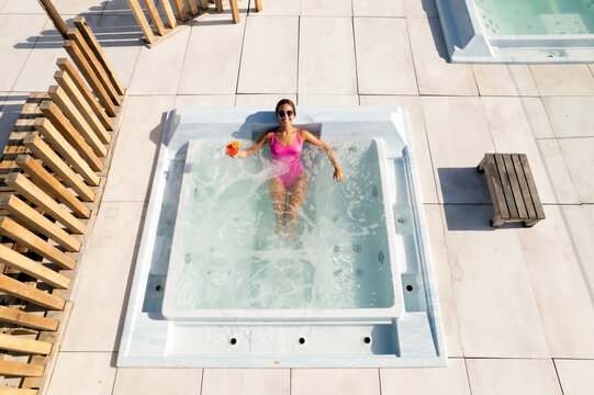 Young woman relaxing in bubble pool on roof top drinking cocktail