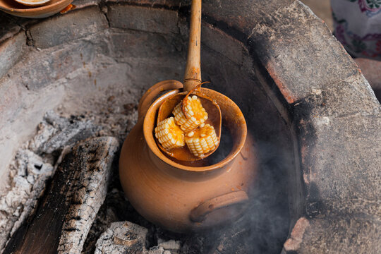 Wooden spoon with 3 pieces of corn on a clay pot
