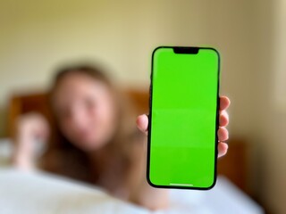 the girl smiles lies in her bed and shows the phone with a green screen can be used to advertise...