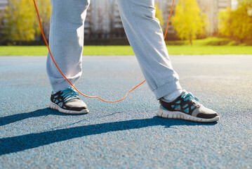 Fitness, aerobics and active lifestyle concept. Close-up of woman jumping on skipping rope, sportswoman exercising on sports field outdoors on sunny day. Low angle view