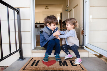 Children sitting on front porch of home with welcome mat