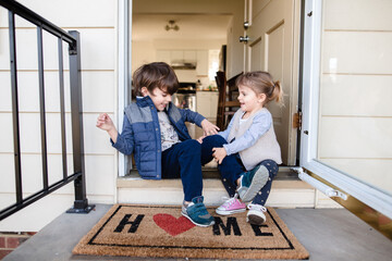 Children sitting on front porch of home with welcome mat