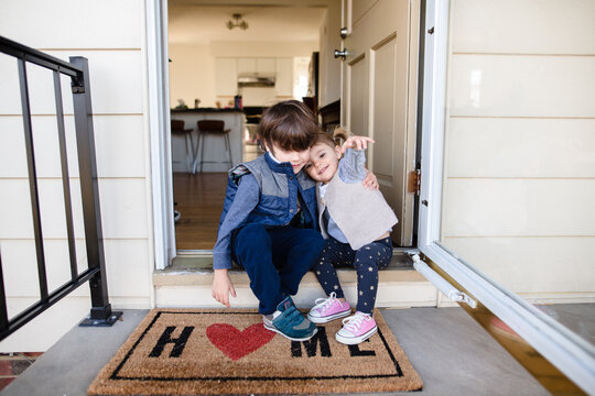 Brother has arm around sister as they sit on stoop