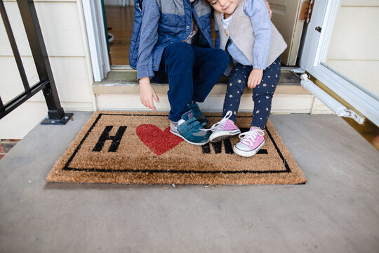 Children sitting on front porch of home with welcome mat