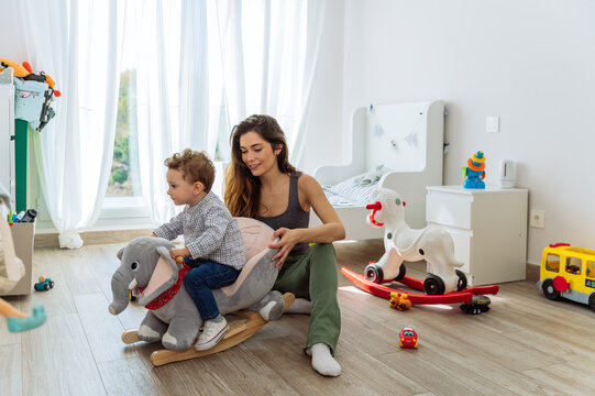 Cute boy on rocking toy in playroom with mother