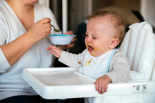 Mother feeding crying baby in kitchen