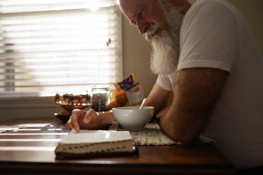 Man reading the bible at kitchen table.