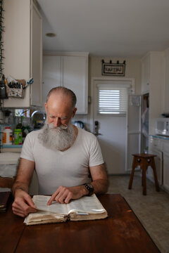 Man reading the bible at kitchen table.