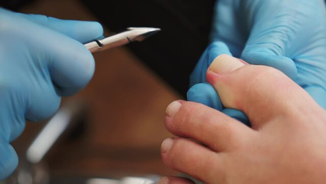Processing of rough cuticles  of nails on leg  with a nail nipper.  Nails care process in nail salon. Manicurist removing cuticles on big toe. Process of pedicure in a beauty salon..