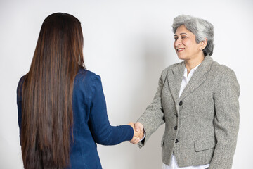 Indian senior corporate female boss hand shake with young business woman having a deal isolated on white studio background,