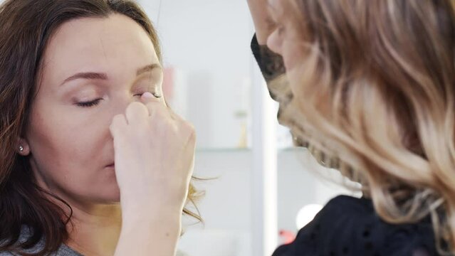 Makeup artist draws the shape of a woman's eyebrows in a beauty salon. Cosmetologist forms the eyebrow line with a black thread on a female face.