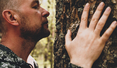 Adult man touches a huge tree, sniffs the bark and hugs the trunk. An adult man enjoys being alone...