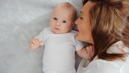 Happy newborn baby with his mother. Healthy newborn baby in a white t-shirt with mom. Closeup Faces of the mother and infant baby. Cute Infant boy and parent, top view. Happy family portrait