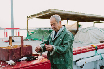 Old man preparing his tools for sewing nets