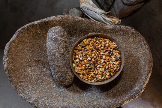 A j&iacute;cara with grains / kernels of corn inside on a stone metate