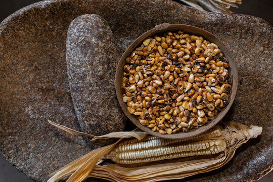 Corn with its leaf and a j&iacute;cara with kernels inside of it on a metate