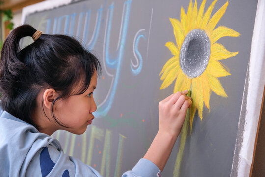 Closeup little asian girl creating chalk drawing on blackboard