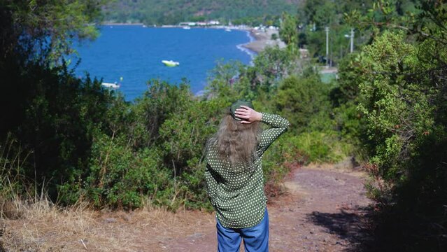 Tourist travels in beautiful marine landscape. 4k stock video footage of rear view of woman on windy warm sunny day standing outside and walking along mountain rural road in Marmaris in Turkey