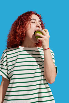 Redhead woman biting fresh apple in studio