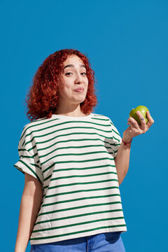 Redhead woman biting fresh apple in studio