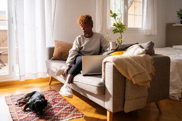 Woman With Laptop Having A Cup Of Coffee At Home Next To Her Dog.