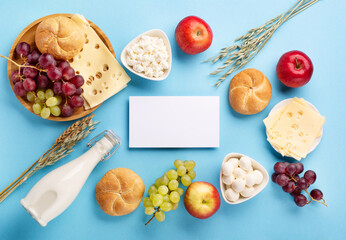 Jewish Shavuot holiday card concept. Dairy products, fruits, cheese, bread, milk bottle on blue background.