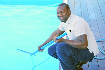 African maintenance pool cleaner during his work. African hotel staff worker cleaning the pool