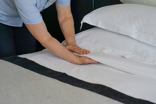 Hand of elderly maid making bed in hotel room. Housekeeper Making Bed
