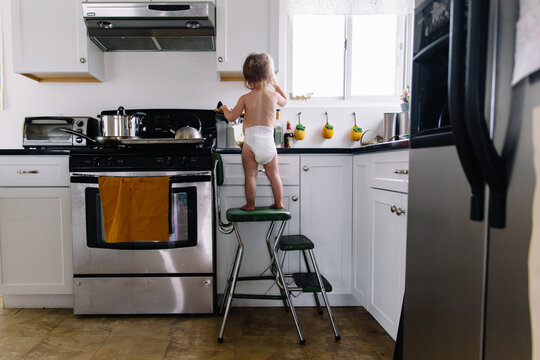 Toddler in diapers stands on kitchen chair to cook