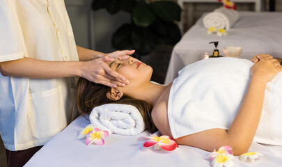 Unrecognizable professional masseuse therapist standing massaging head and face of Asian young...