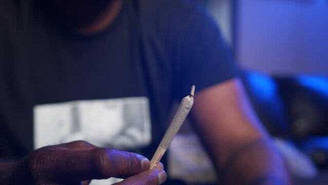 African american black man holding a marihuana cannabis joint before smoking weed on a sofa. Close up