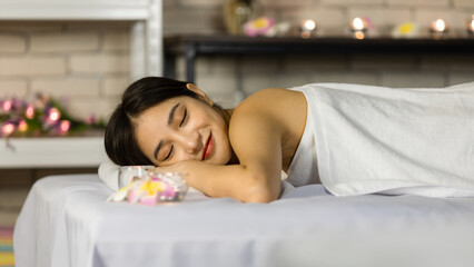 Obraz na płótnie Canvas Closeup Asian young beautiful sexy happy female spa customer covered by white clean bath towel laying down resting relaxing closed eyes smiling on massaging bed putting bloom orchid flower on ear