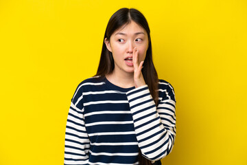 Young Chinese woman isolated on yellow background whispering something with surprise gesture while looking to the side