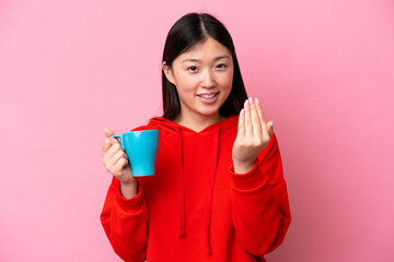 Young Chinese woman holding cup of coffee isolated on pink background inviting to come with hand. Happy that you came