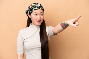 Young Chinese woman isolated on beige background pointing away