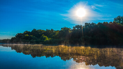 Aerial  view of a beautiful summer  landscape over river while dawn. Top view over river with a smooth water surface reflecting blue sky. Morning evaporation on a river while sunrise.